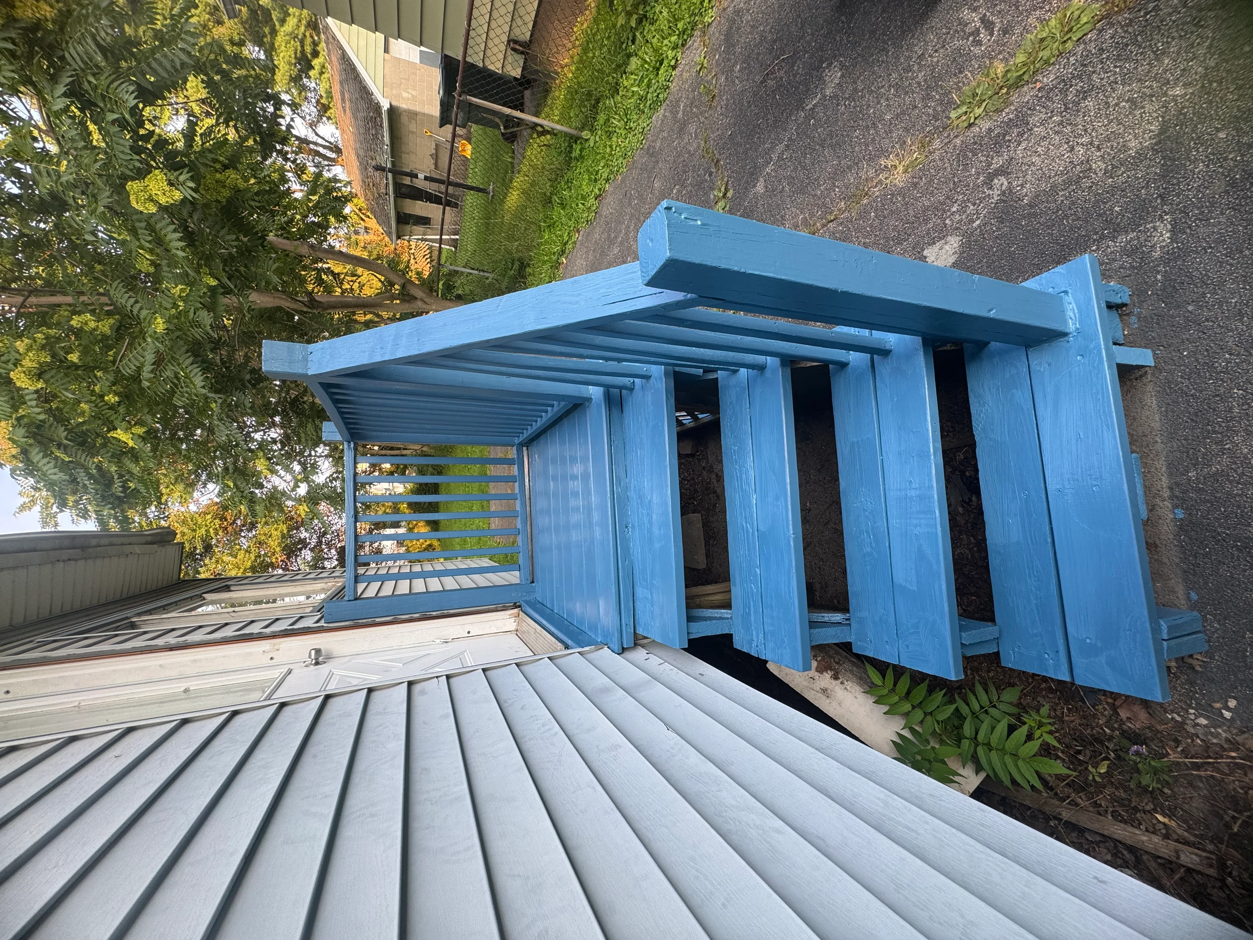 Blue metal pergola with horizontal slats and vertical louver panels over composite deck