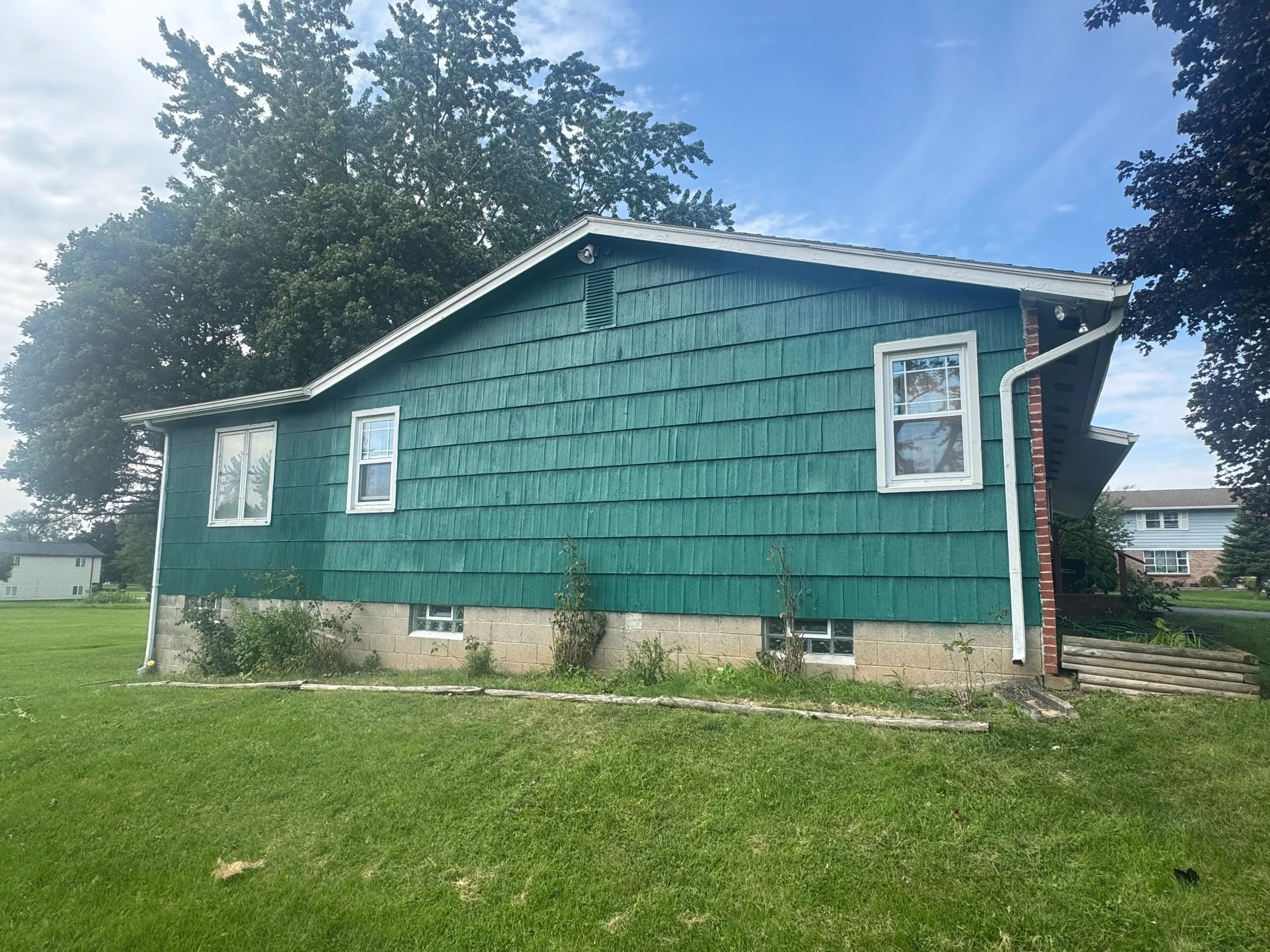 Teal vertical shingle siding with white trim, new windows, and concrete foundation on residential home