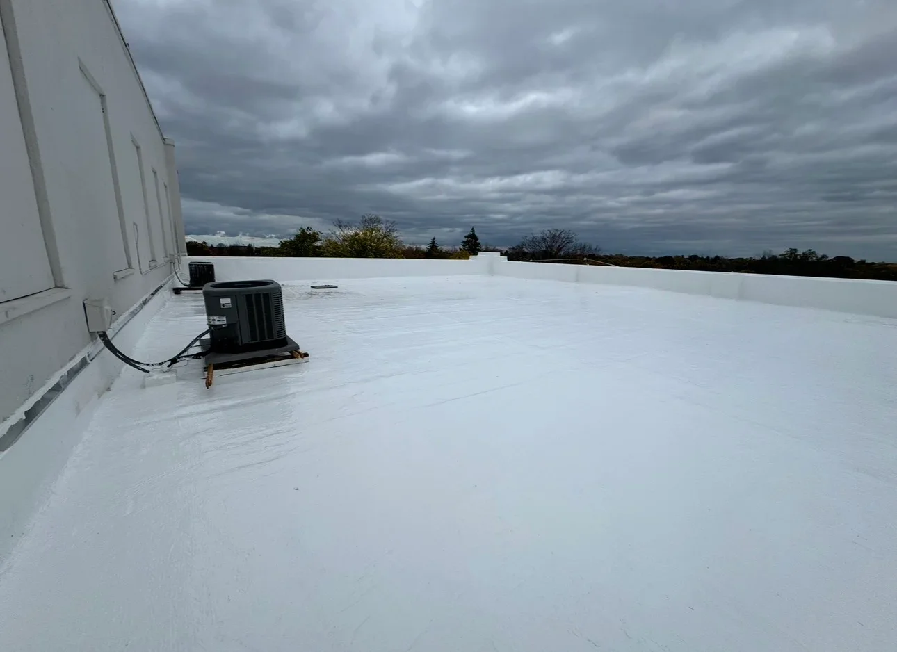 White flat roof membrane with mounted HVAC unit and parapet wall edge detail