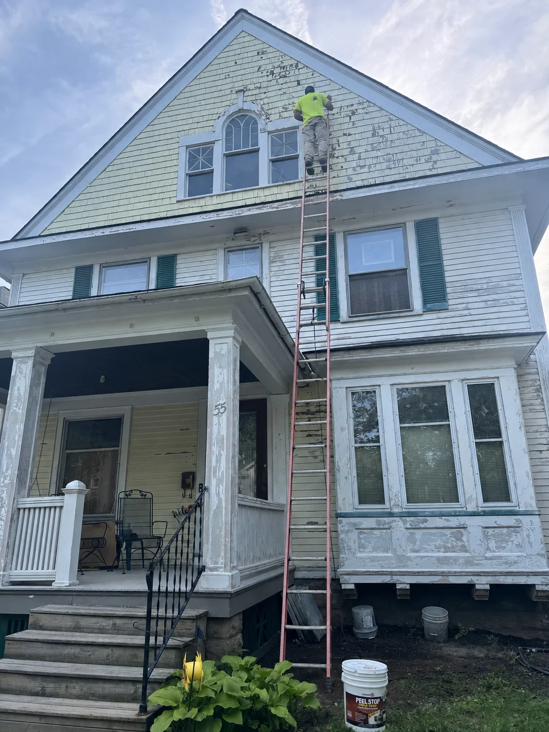 Worker on ladder installing new shingles on gable end of colonial home with white trim